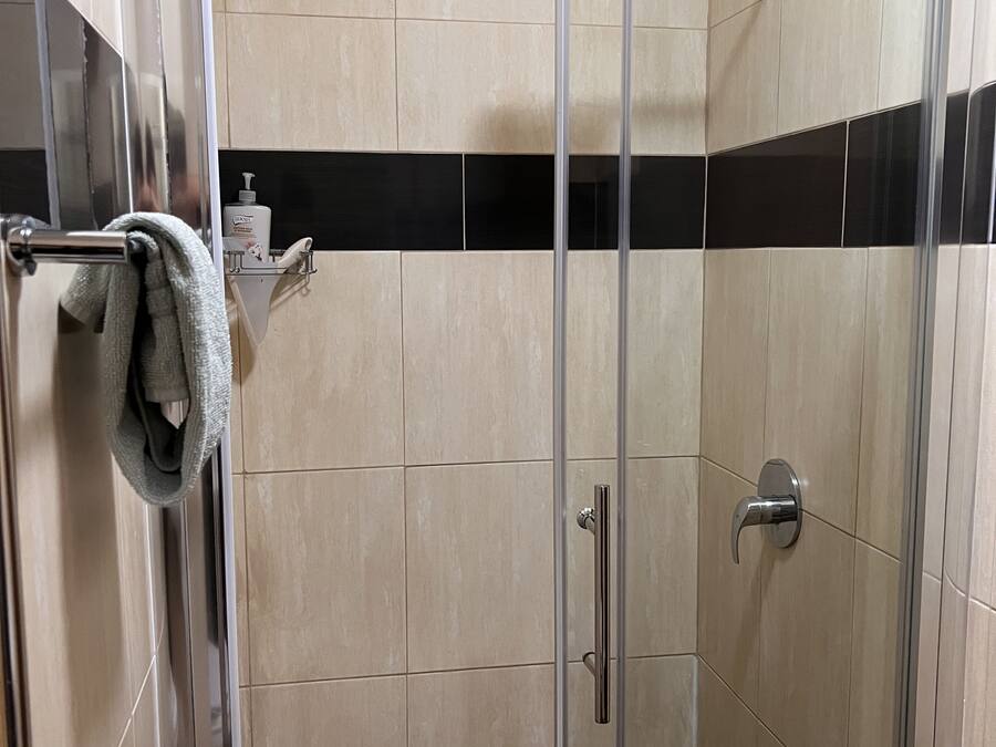 Una ducha con cerramiento de vidrio, baldosas color beige y una franja horizontal negra.