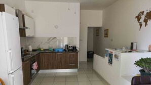 A modern kitchen with a central island, white cabinets, and a dining area with a table and chairs. - All Nations Holiday Home (Ghajnsielem)