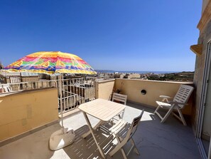 Ein Balkon mit Tisch und Stühlen, einem bunten Sonnenschirm und Blick aufs Meer.