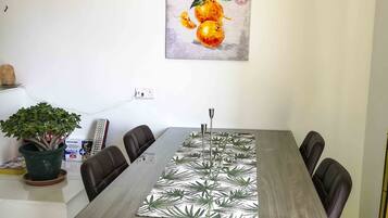 Un comedor con una mesa larga, seis sillas, una planta en maceta y un cuadro en la pared.