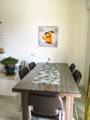 A dining area with a long table, six chairs, a potted plant, and a painting on the wall. - All Nations Holiday Home (Ghajnsielem)