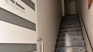 A staircase with blue and white patterned tiles, a metallic handrail, and a door with a logo and text. - All Nations Holiday Home (Ghajnsielem)