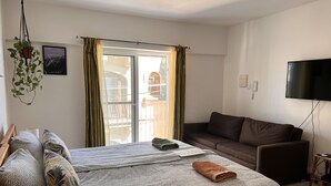 A bedroom with a bed, a brown sofa, a TV, and a window with curtains. - All Nations Holiday Home (Ghajnsielem)
