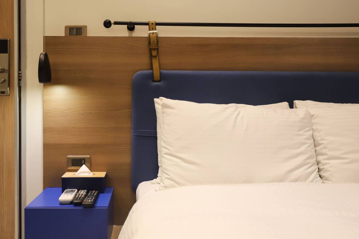 Habitación de hotel con cabecera de madera, mesita de noche con control remoto y caja de pañuelos.