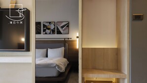 Une chambre à coucher moderne avec un lit, une table de chevet et un téléviseur fixé au mur. Des tableaux abstraits sont accrochés au-dessus du lit et un meuble en bois se trouve en dessous.