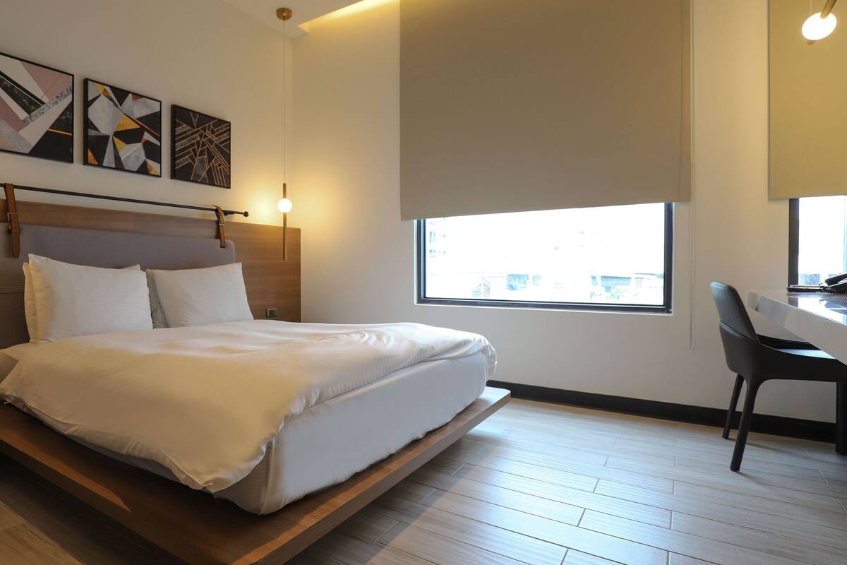 Una habitación de hotel moderna con una cama, un escritorio y un ventanal grande.
