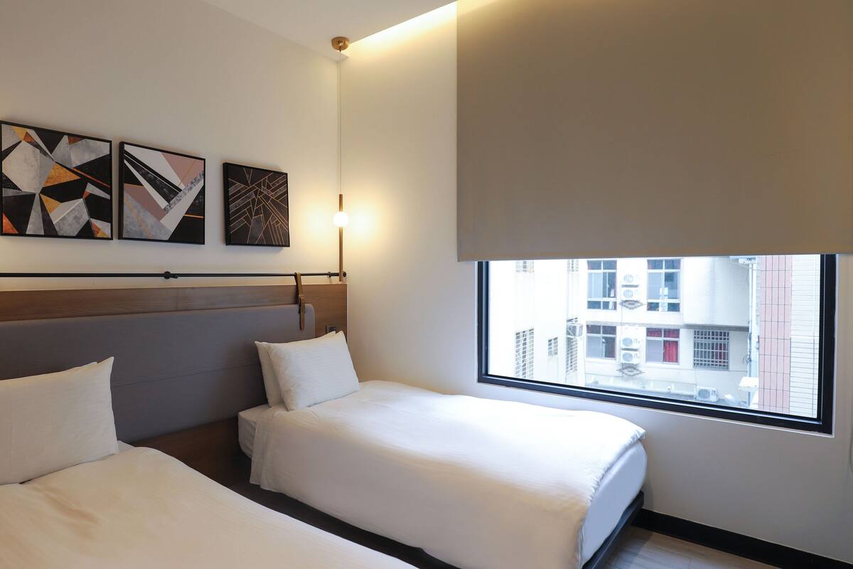 Habitación de hotel con dos camas, un ventanal grande y un cuadro abstracto en la pared.