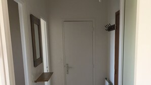 Un pasillo con una puerta blanca, un estante pequeño y un radiador a la derecha.