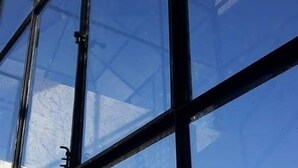 Se ve claramente el cielo y la estructura de un edificio reflejados en un ventanal con marco de metal.