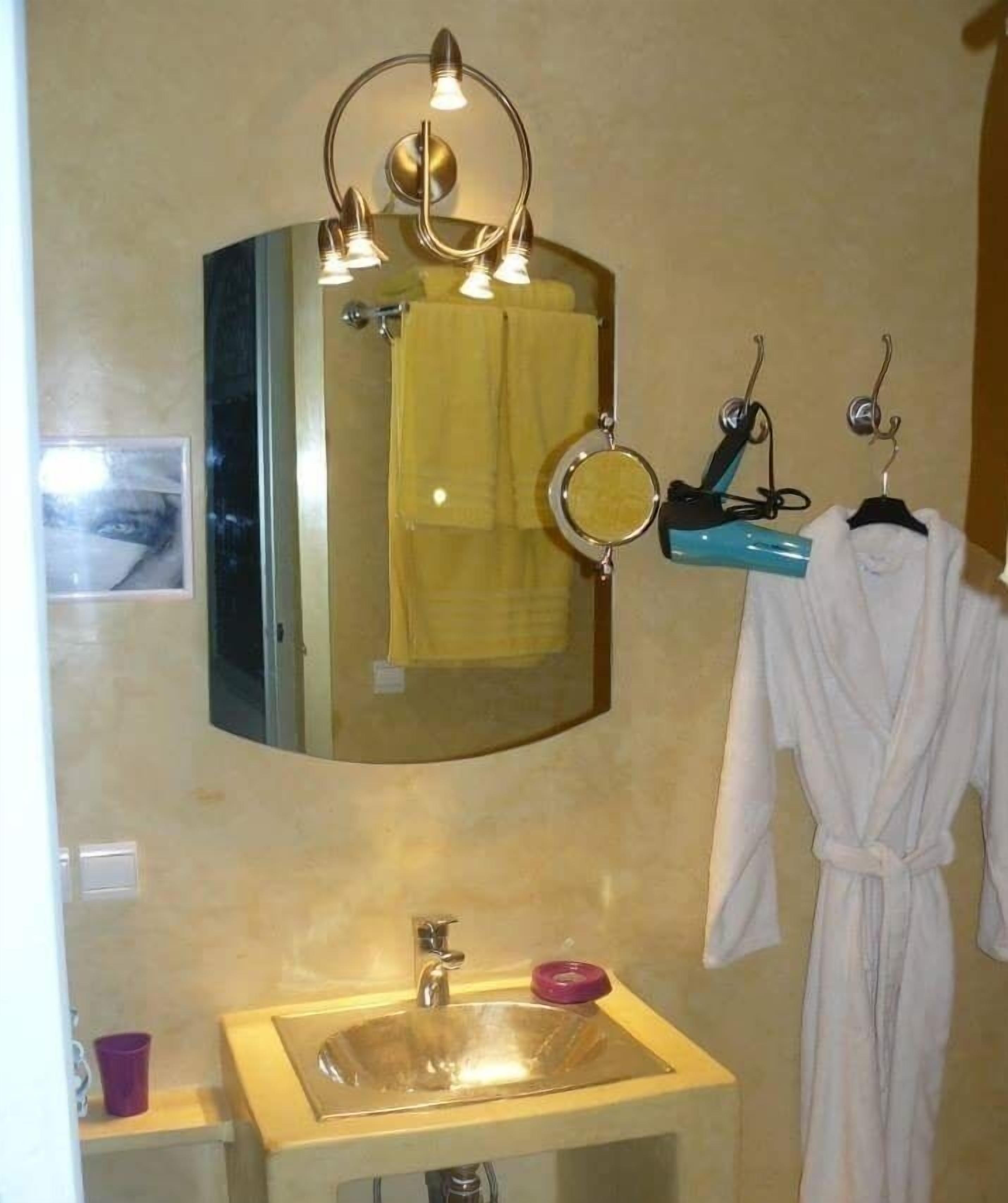 A bathroom with a sink, mirror, towel rack, and robe hanging.