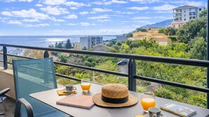 Una mesa en el balcón con vista al mar, un sombrero de paja y un libro.