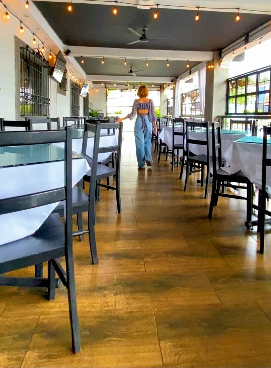 A restaurant with tables and chairs arranged in rows, a ceiling fan, and string lights.