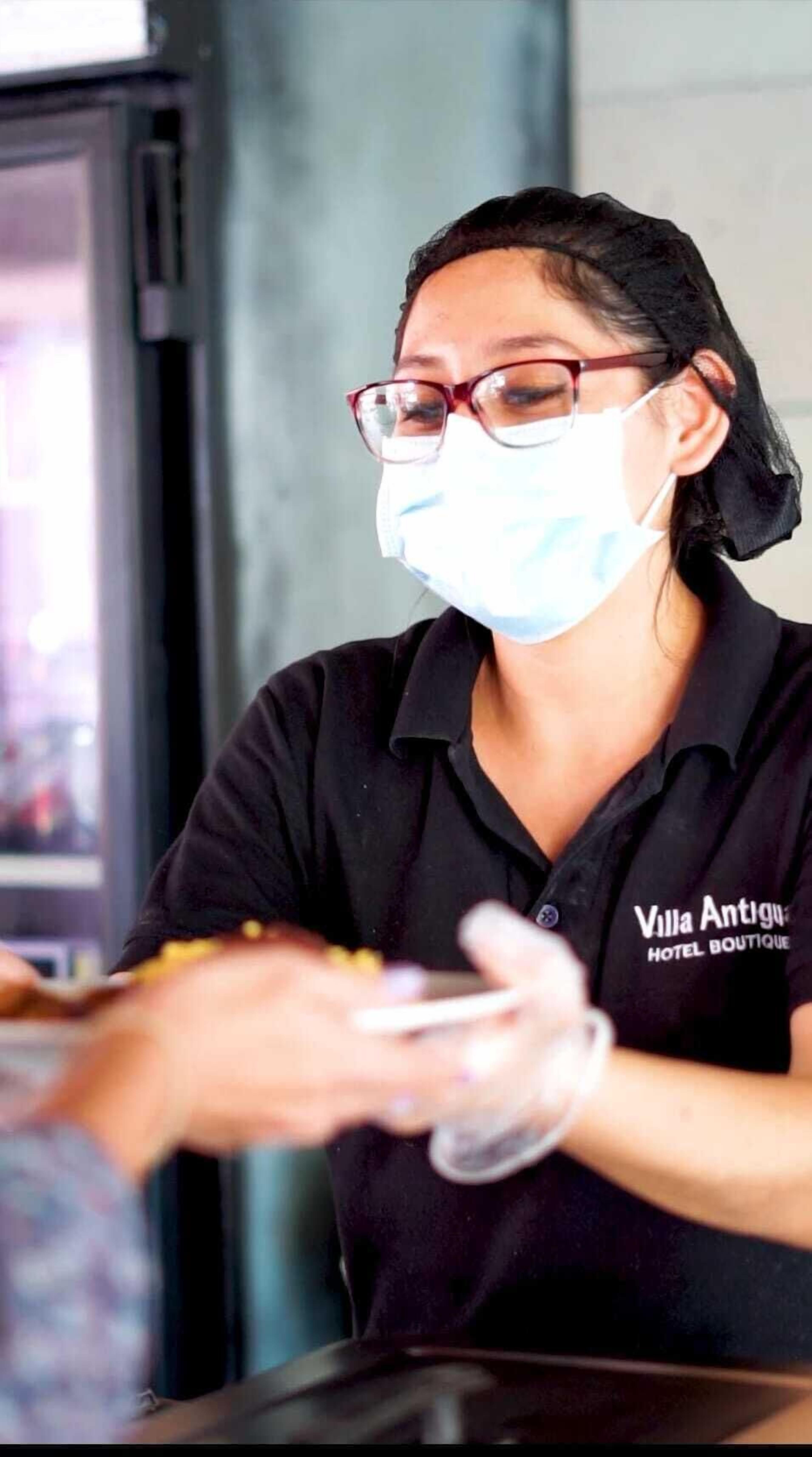 A person wearing a black shirt with "Villa Antiguo Hotel Boutique" printed on it, handling a card or ticket at a counter.