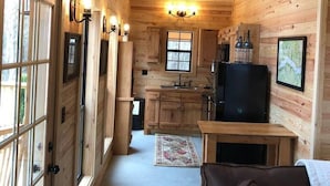 A log cabin interior with a kitchen, dining area, and a large window. - Cabins At Midway, Tombigbee (Fulton)