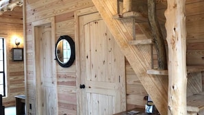 A wooden interior with a spiral staircase, a door with a round mirror, and a small wooden cabinet. - Cabins At Midway, Tombigbee (Fulton)