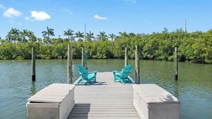 A dock with two chairs and a table, surrounded by water and palm trees. - 4Bdm Waterfront Home w/ Heated Pool, Walk to Beach (Indian Rocks Beach)