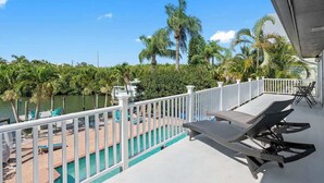 A balcony with a pool, lounge chairs, and a view of a lake and palm trees. - 4Bdm Waterfront Home w/ Heated Pool, Walk to Beach (Indian Rocks Beach)