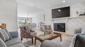 A modern living room with a fireplace, comfortable seating, and a large TV. - 4Bdm Waterfront Home w/ Heated Pool, Walk to Beach (Indian Rocks Beach)