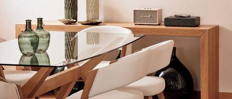 A modern dining area with a glass table, white chairs, and a wooden sideboard with decorative items and a speaker.