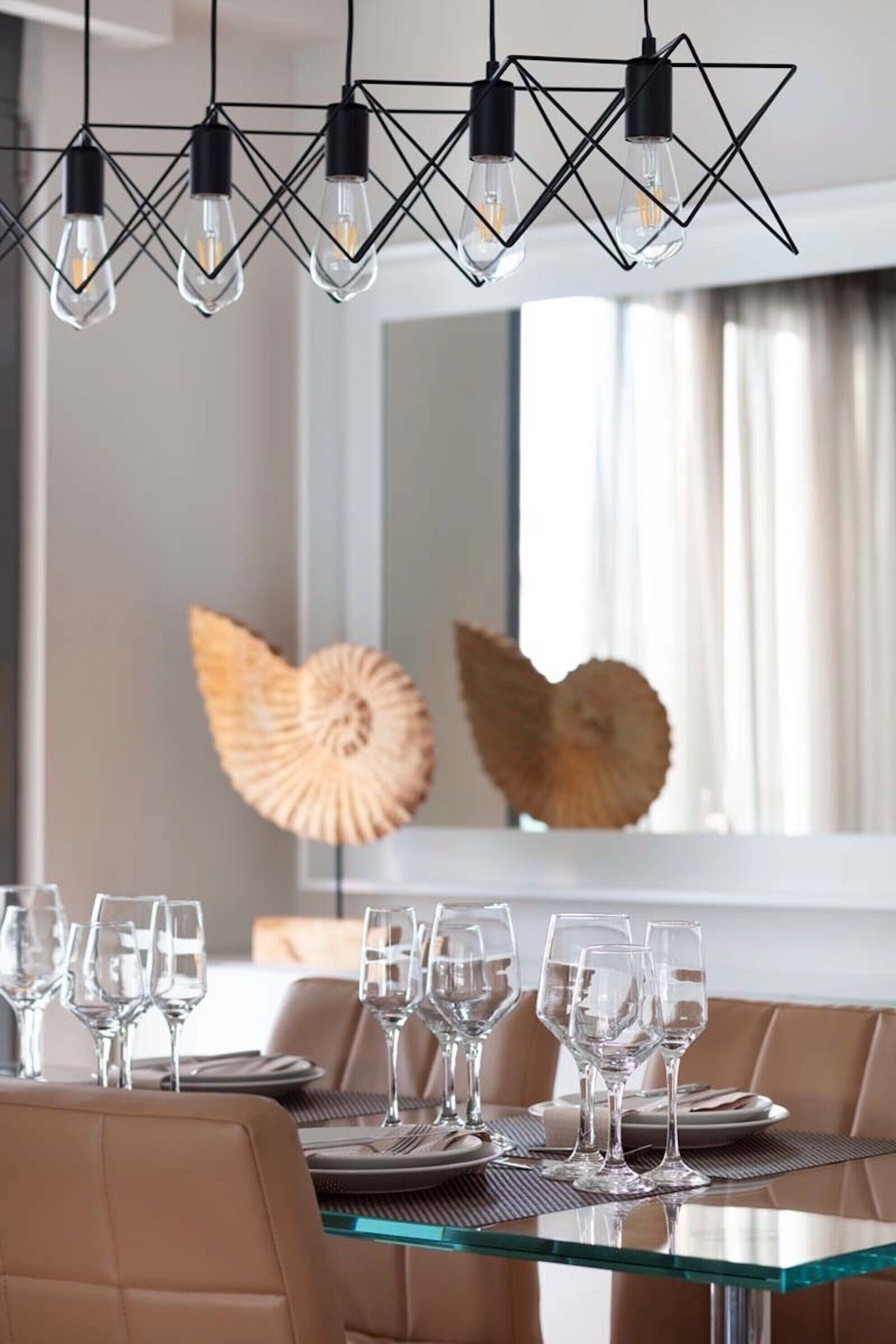 Un coin repas avec une table en verre dressée pour six personnes, entourée de fauteuils en cuir. Au-dessus de la table, on trouve trois suspensions au design géométrique.