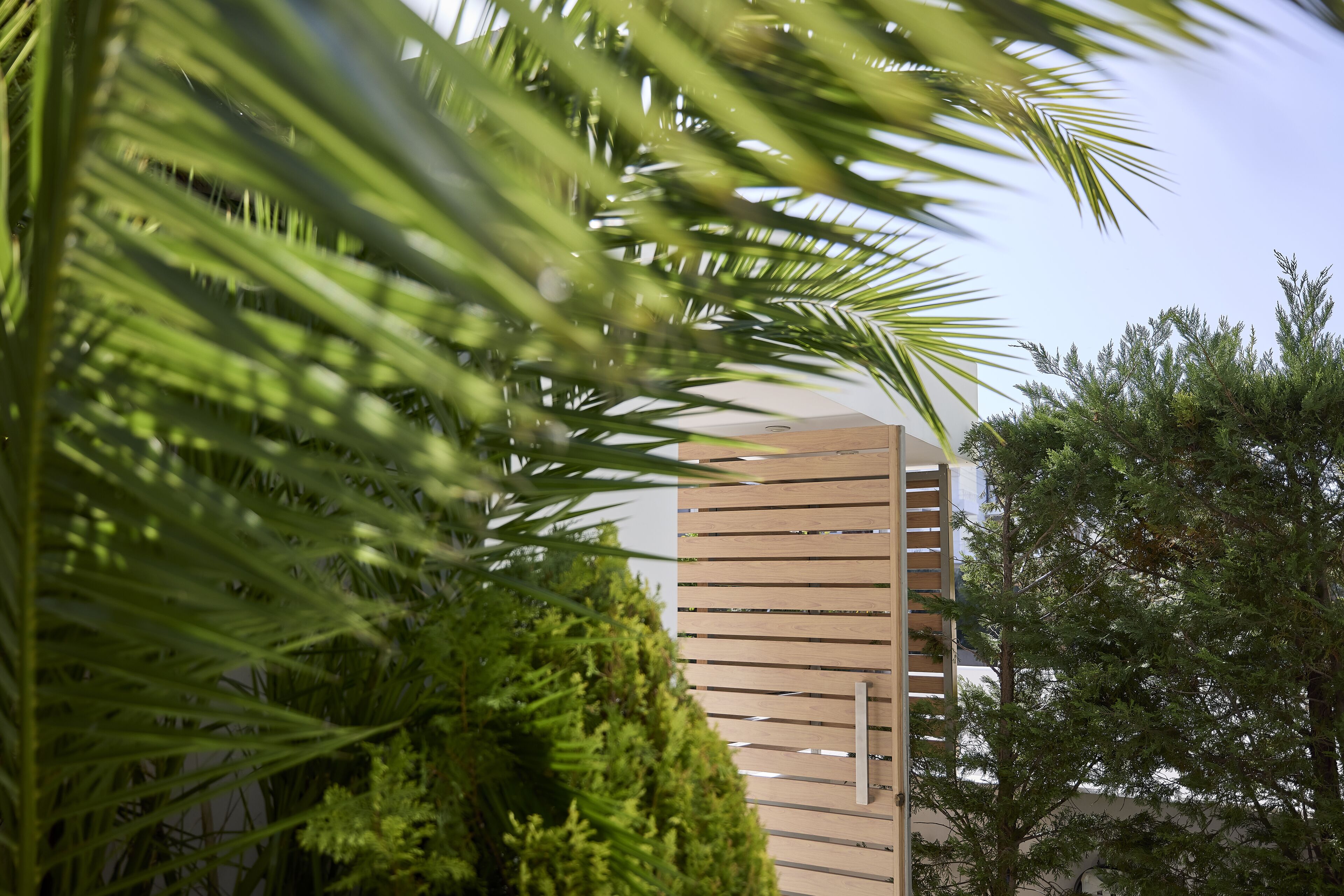 A building with a modern design, surrounded by lush greenery including palm trees and dense bushes.