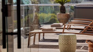 Una terraza de madera con barandilla de cristal, una planta en maceta, una mesa redonda y dos sillas.