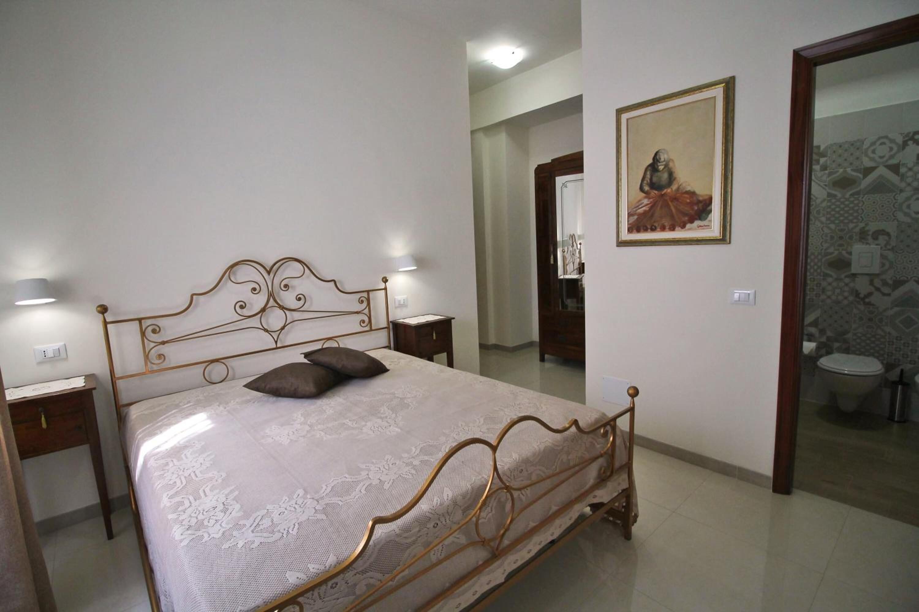 A bedroom with a bed, nightstands, a painting, and a bathroom visible through an open door.