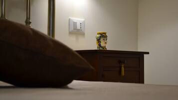 Un dormitorio con cabecera de madera, una mesita de noche con un florero decorativo y un enchufe de pared.