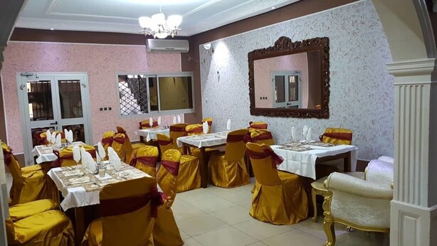Uma área de refeições com mesas dispostas para um evento formal, com capas douradas nas cadeiras e toalhas brancas.