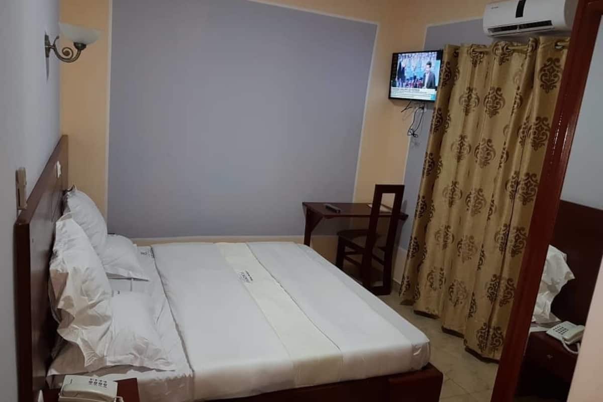 A hotel room with a bed, a desk, a chair, a TV mounted on the wall, and a curtain.