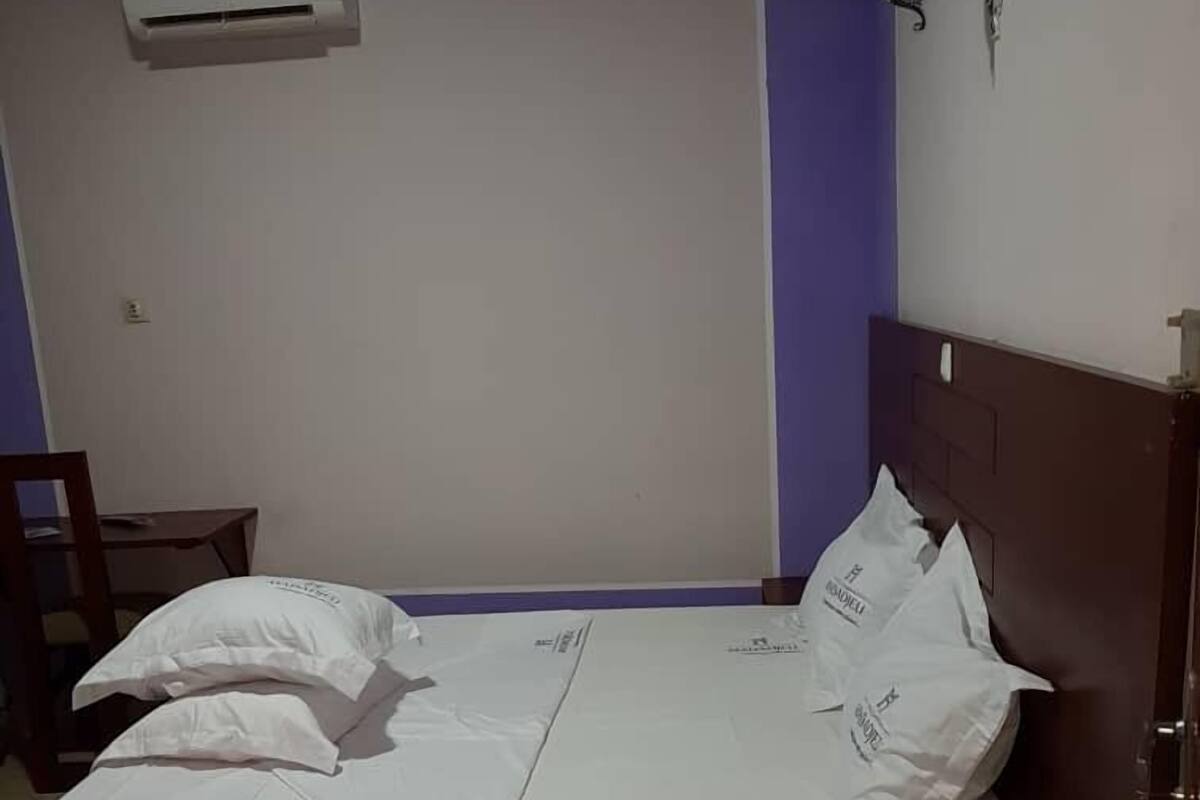 A single bed with white bedding, a wooden headboard, and a small bedside table with a phone.