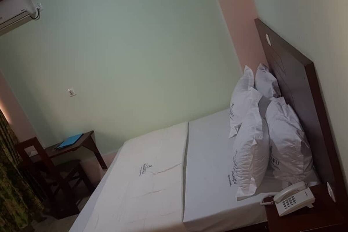 A hotel room with a bed, a bedside phone, and a desk with a chair.