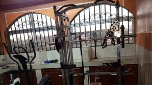 Uma academia com diversos equipamentos de exercício, incluindo suporte para agachamento, halteres e uma máquina elíptica.