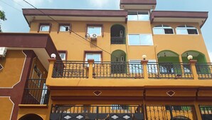 Um edifício de vários andares com varandas, aparelhos de ar condicionado e entrada fechada por portão.