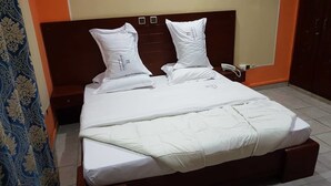 Uma cama com roupa de cama branca e duas almofadas, cabeceira de madeira e telefone ao lado da cama.