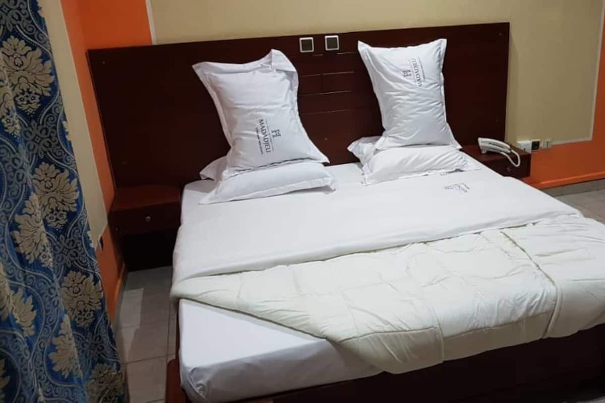 A bed with white bedding and two pillows, a wooden headboard, and a bedside telephone.