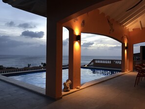Un espace piscine offrant une vue sur l’océan, un coin salon abrité et une sculpture en pierre.