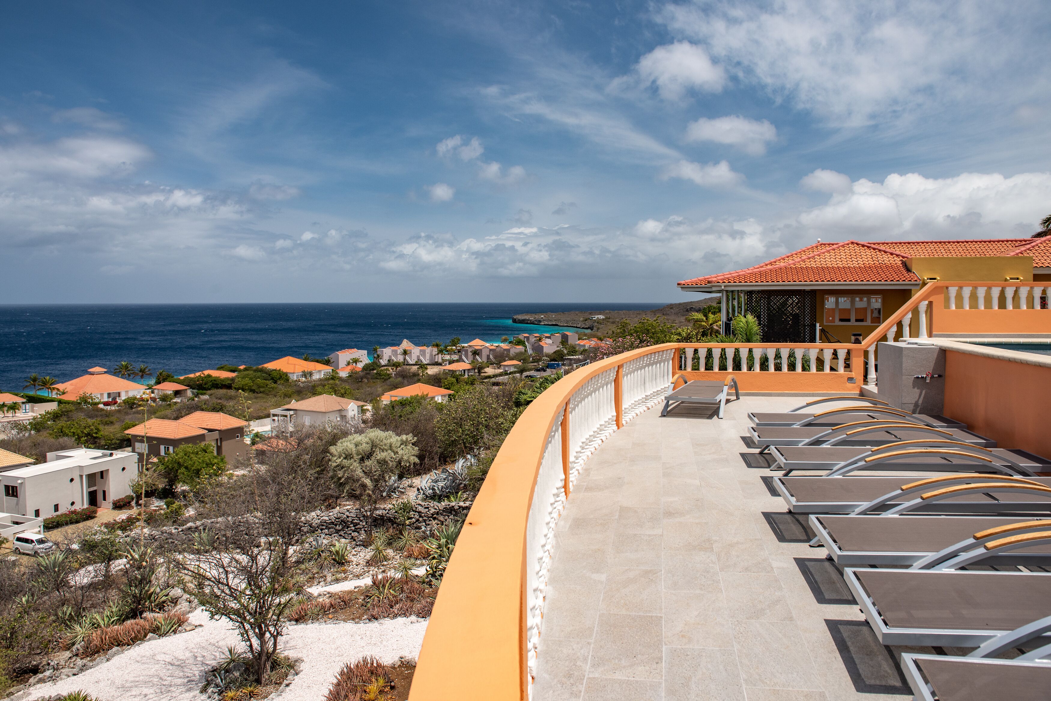 Un complexe hôtelier doté d’un balcon incurvé donnant sur l’océan, avec des chaises longues et une vue sur la mer et les autres bâtiments.