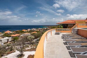A resort with a curved balcony overlooking the ocean, featuring sun loungers and a view of the sea and other buildings. - Stunning ocean view villa with private pool (Sint Willibrordus)