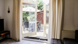 Een kamer met een schuifdeur die leidt naar een terras buiten, met een tafel en stoelen.