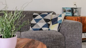 Een grijze bank met gekleurde kussens, een houten bijzettafeltje en een potplant.