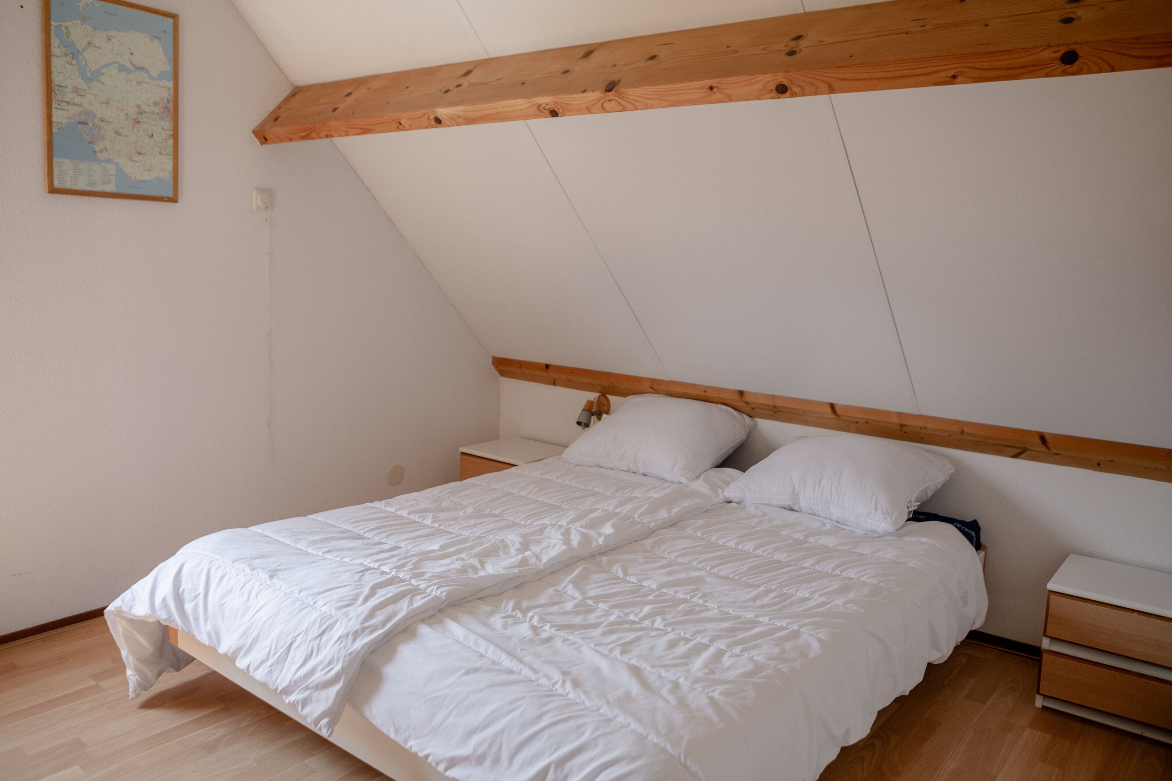 A bedroom with a wooden ceiling, a white bed, and a nightstand.