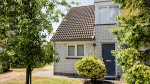 Een twee verdiepingen tellend huis met een pannendak, een voordeur en een kleine voortuin met een boom en een struik.