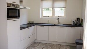 Een moderne keuken met witte kastjes, een zwart aanrecht, een ingebouwde oven, een raam met zonwering en een spoelbak.