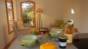 Comedor con una mesa dispuesta para dos personas, que incluye una botella de vino, una hogaza de pan y un bol de fruta.
