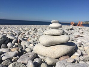 Une pile de pierres lisses et arrondies sur une plage de galets, avec un ciel bleu dégagé et une mer calme en arrière-plan.