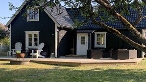 Een zwart huis met een terras, witte stoelen en een bloempot.