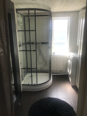 Eine Eckdusche mit Glastüren, eine Waschmaschine und ein Fenster mit Tageslicht.