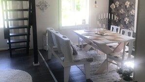 Een eethoek met een witte tafel en stoelen, een zwarte trap en een wand bedekt met bloemenbehang.