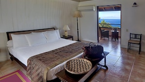 A hotel room with a bed, a view of the ocean, a balcony with a table and chairs, and a luggage rack. - Luxury Villa | Private Infinity Pool + Ocean View (Black Rock)